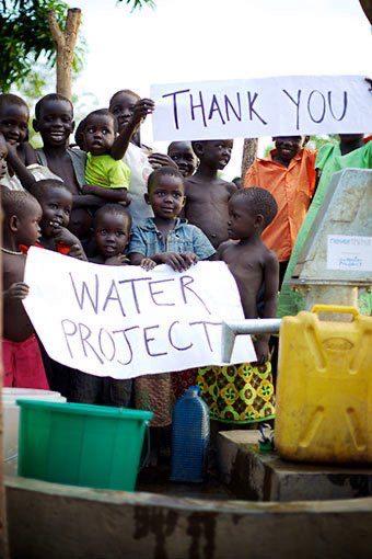 Children holding thank you signs at a water project site with yellow water containers